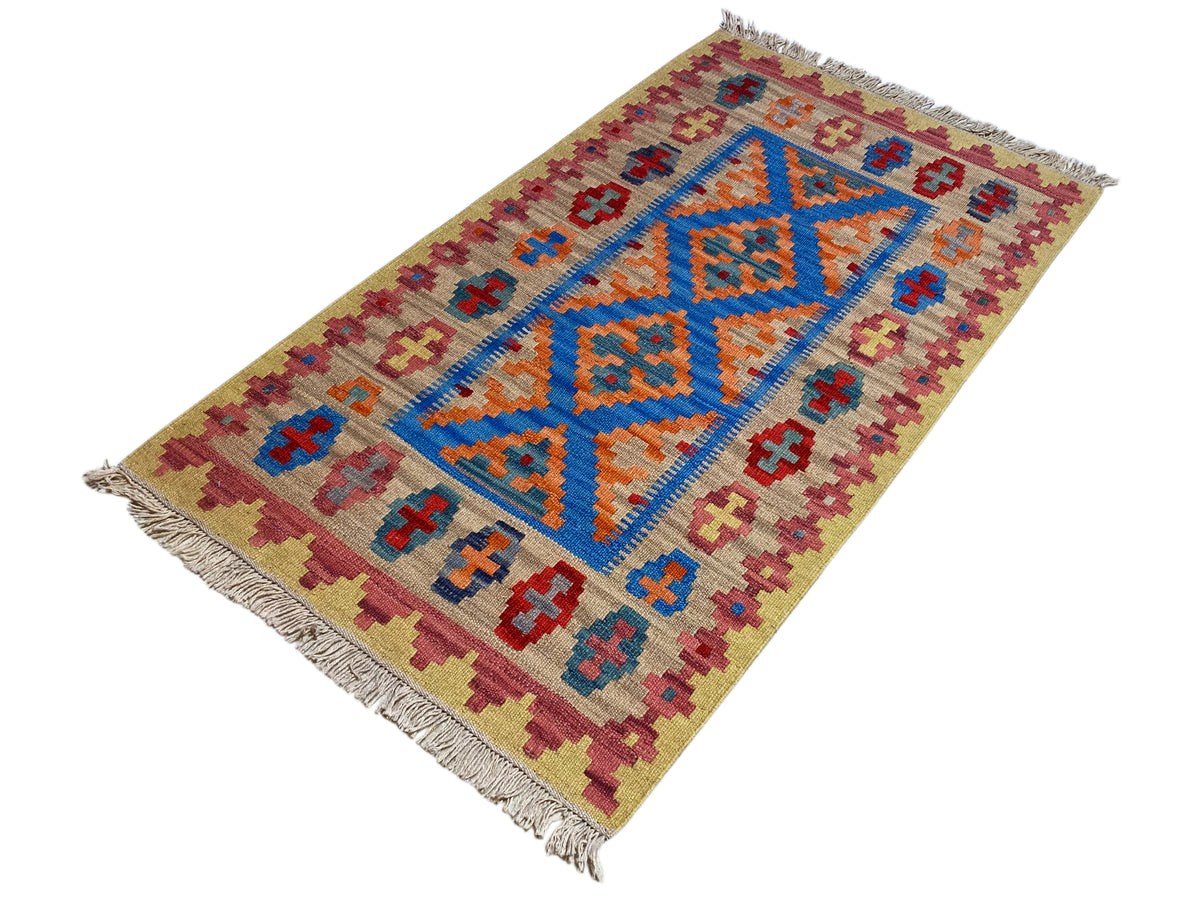 Beige kilim rug with a blue cross and ornamental pattern, orange accents, and fringes