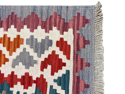 Detail view: multicolored cross and diamond patterns on a kilim rug, with fringes