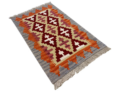 Kilim rug, photographed at an angle: light gray base pattern with orange, cream, and red