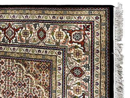 Brown Indo-Tabriz carpet border detail with colorful ornaments and fringe on the right