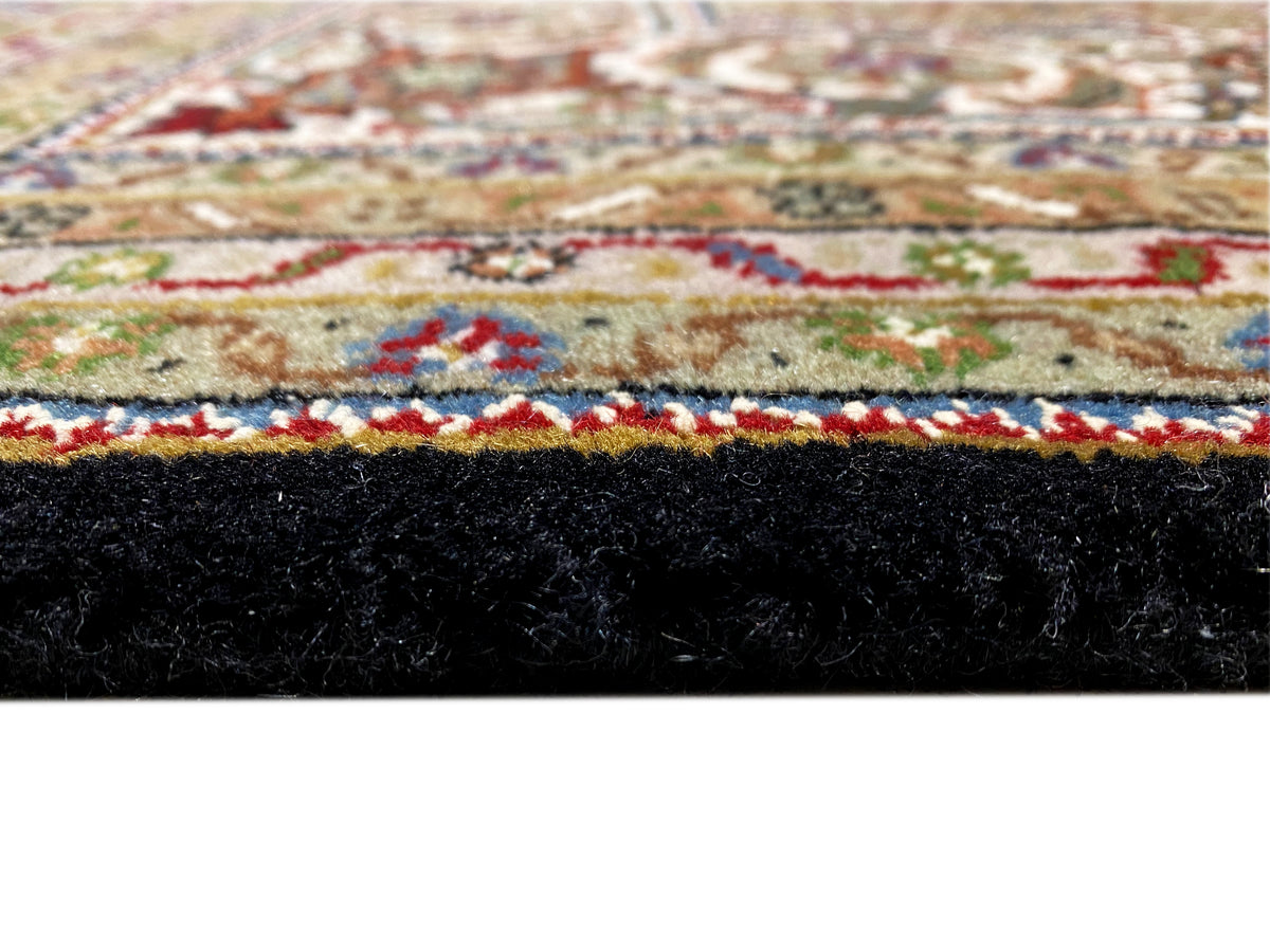 Close-up: Brown Indo-Tabriz rug with a colorful ornamental border and fringes.