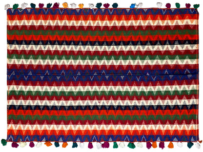 Close-up: rug with a striped pattern in blue, green, and red, with tassels along the edge
