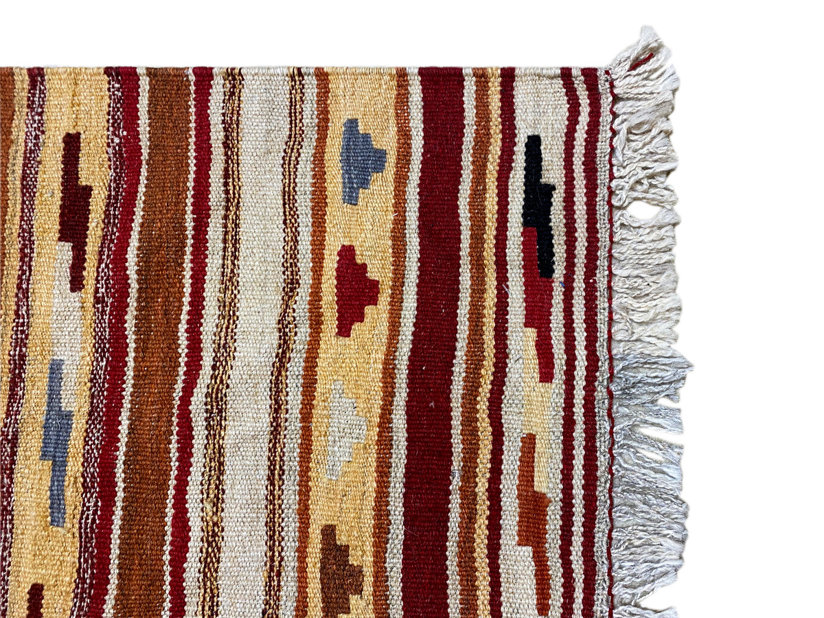 Close-up of a kilim rug: striped ornaments, white textile fringes along the edge