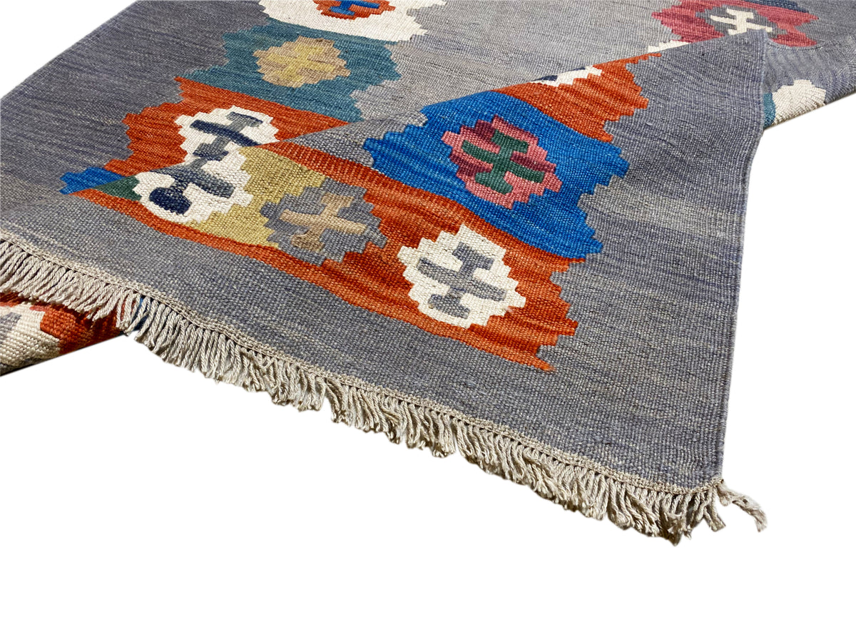 Gray mottled kilim rug, view of a corner with colorful diamonds and fringes