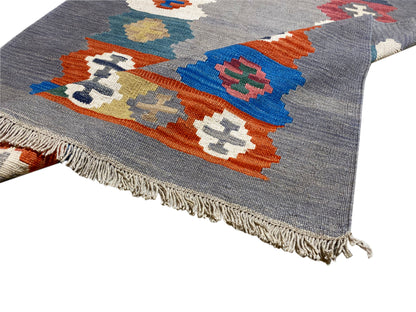 Gray mottled kilim rug, view of a corner with colorful diamonds and fringes
