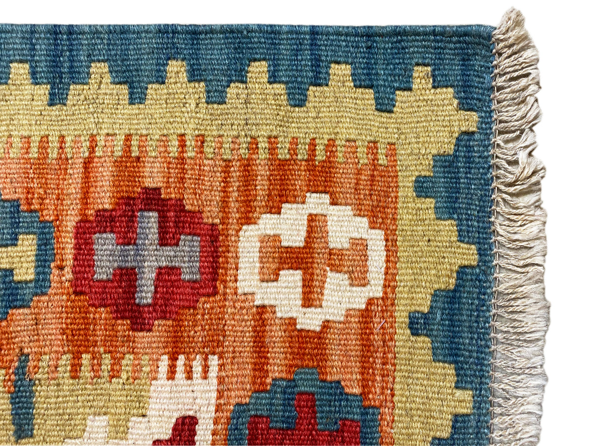Kilim rug corner detail with a blue border, fringe, and orange-yellow color fields