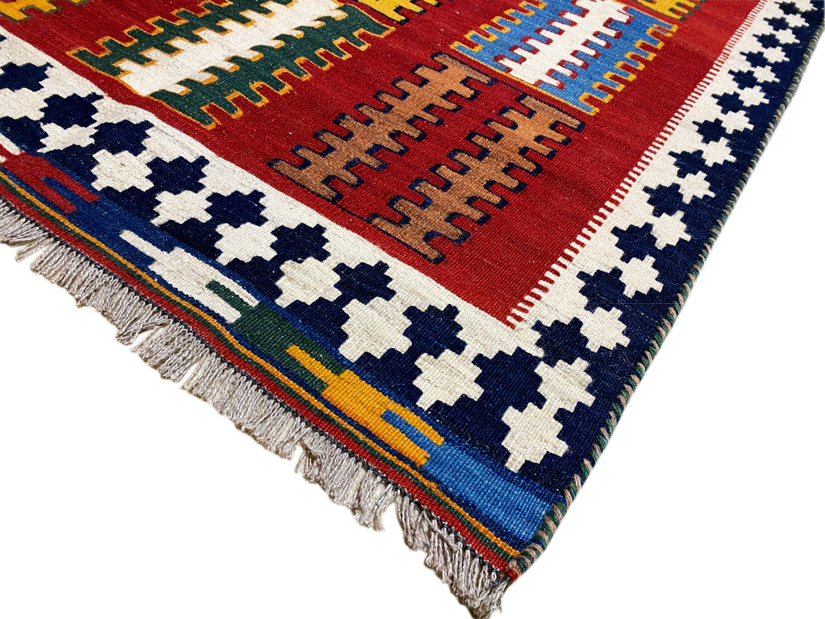 Kelim rug from the corner: red field, blue-and-white cross motifs, and a multicolored border frieze