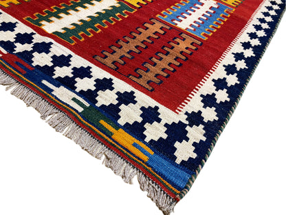 Kelim rug from the corner: red field, blue-and-white cross motifs, and a multicolored border frieze