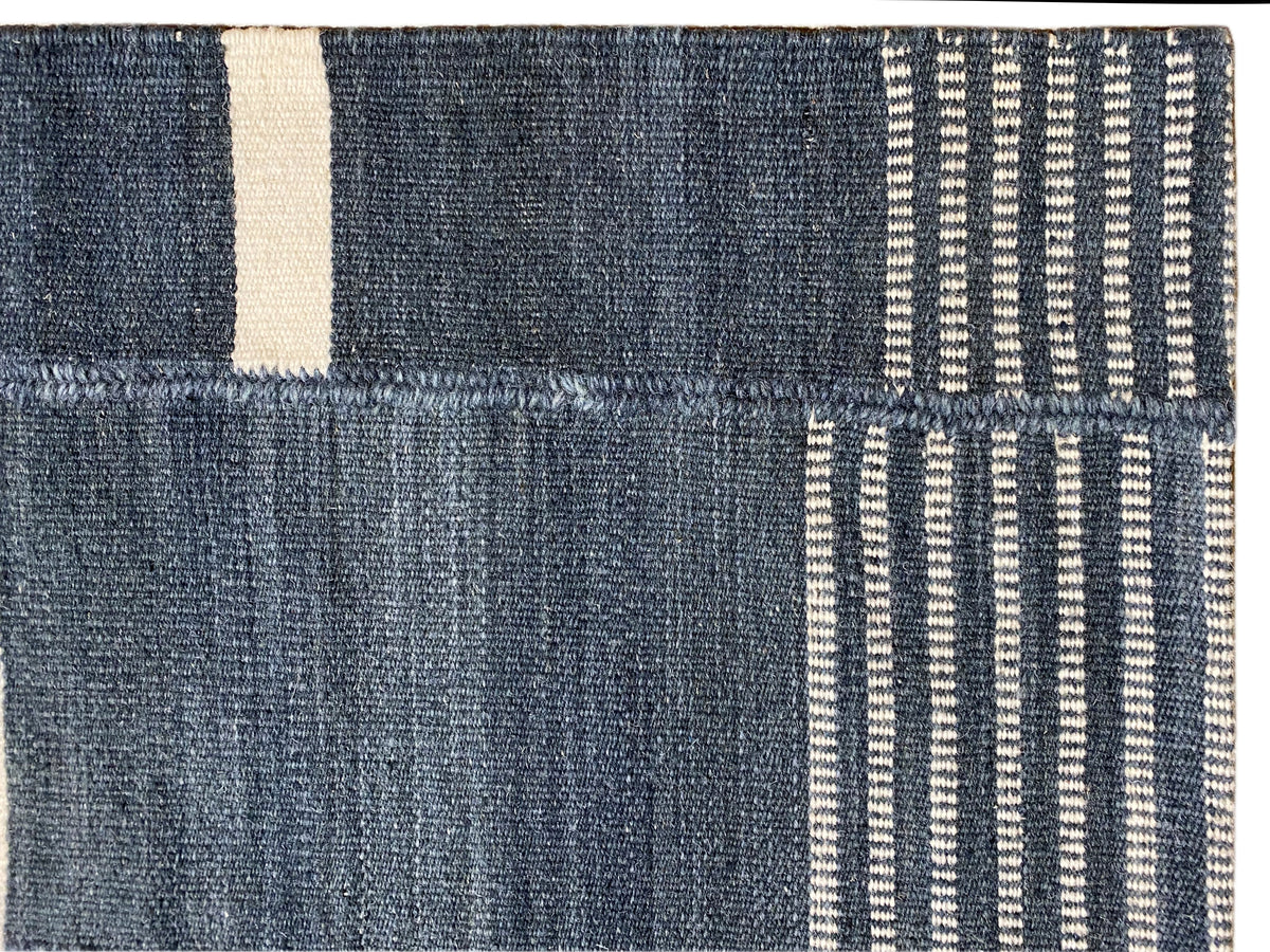 Detail vom Kelim-Teppich: dunkelblaue Flächen, beiger Rand und feine Streifenstruktur