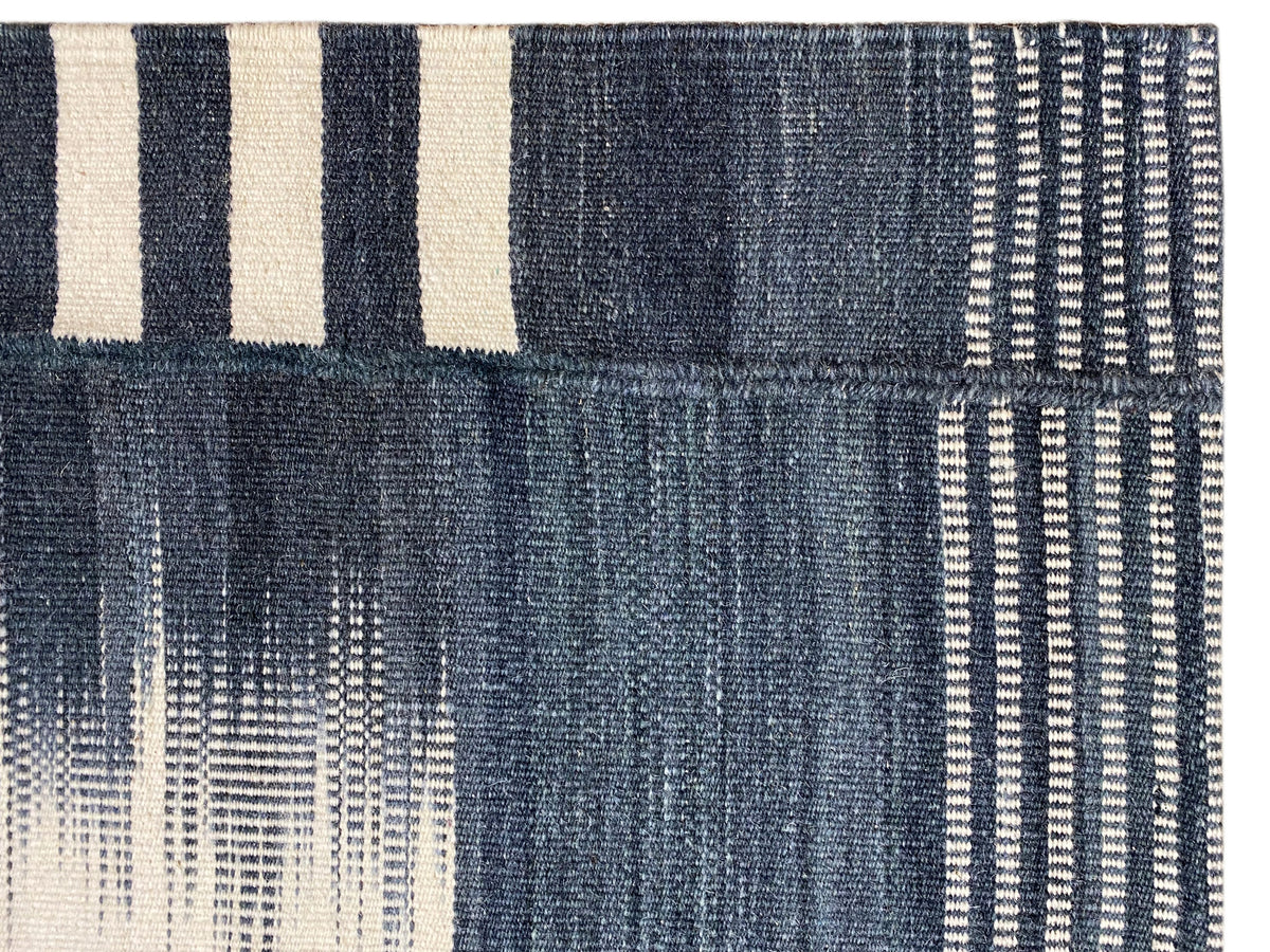 Close-up of a kilim rug: dark blue with white stripes and a woven texture