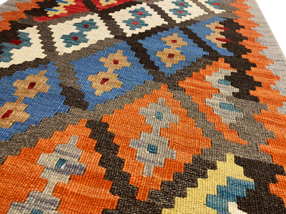Close-up of a kilim rug: orange, blue, cream, and black diamonds on a gray background, fringes