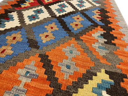 Close-up of a kilim rug: orange, blue, cream, and black diamonds on a gray background, fringes
