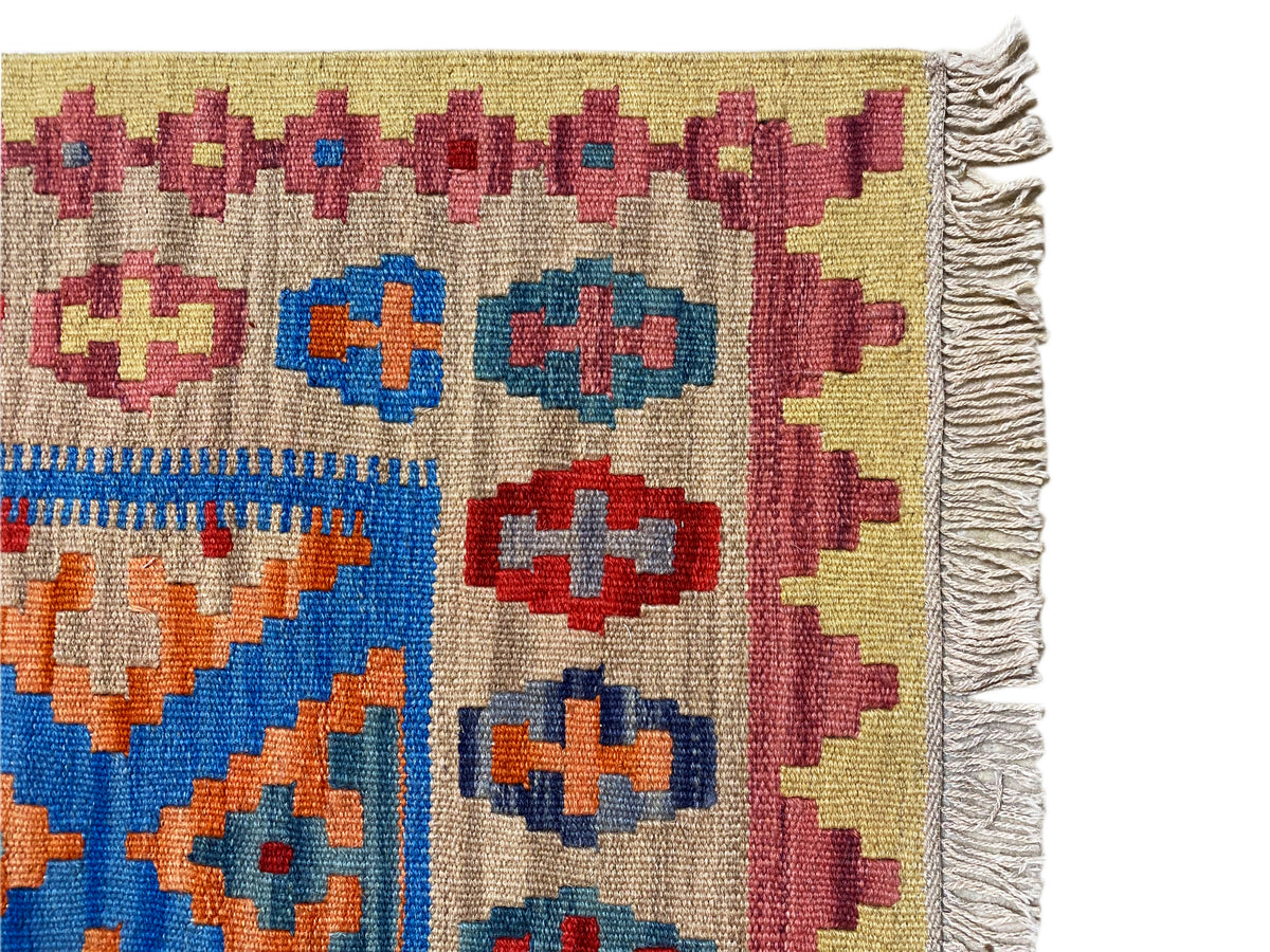 Kilim rug detail with twisted fringe on the right and a colorful geometric pattern on a beige background