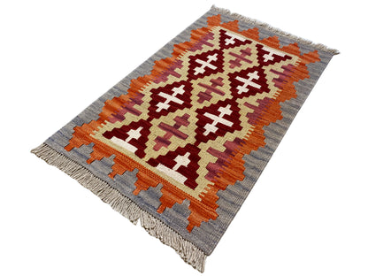 Kilim rug in landscape orientation with cross and diamond patterns in orange, cream, and gray