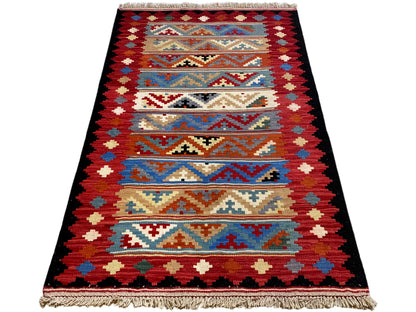 Triangular-looking kilim rug with geometric stripes, shades of red and blue, and fringes.