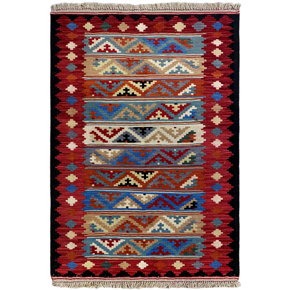 Kilim rug with a symmetrical pattern in red, blue, and beige, with fringes along the edge.