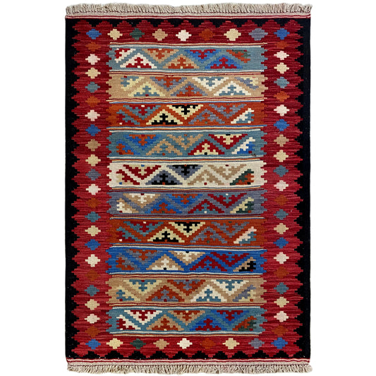 Kilim rug with a symmetrical pattern in red, blue, and beige, with fringes along the edge.