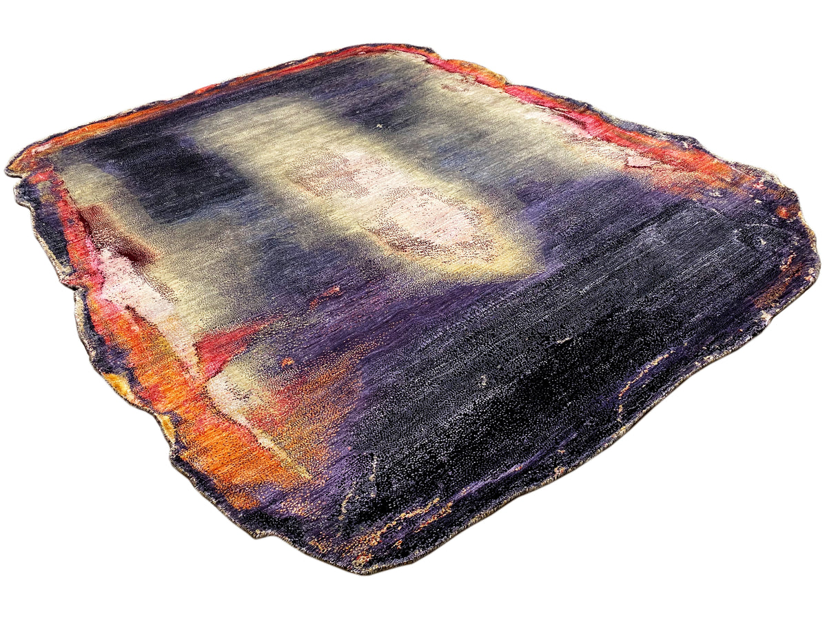 Designer rug with an irregular shape and abstract interplay of dark blue, purple, cream, and orange.
