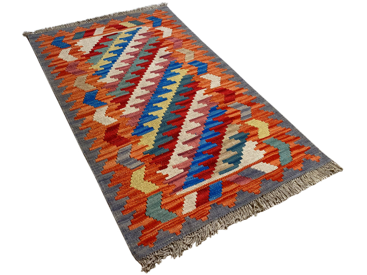 Kilim Qashqai rug viewed at an angle: orange and blue zigzag patterns on a gray background, 121x78 cm