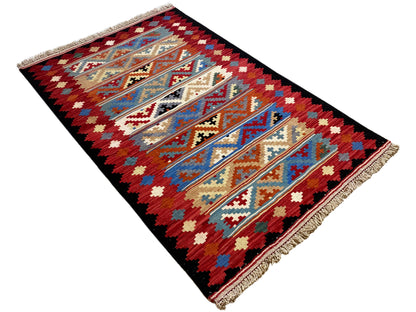 Kilim rug in an angled view: striking red-and-blue pattern with fringes along the edge.