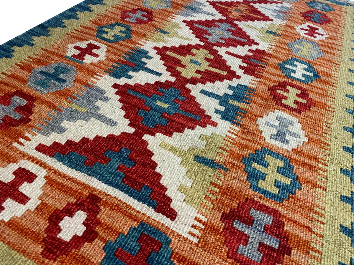 Close-up of a kilim rug: Cross and diamond motifs in orange, blue, and cream
