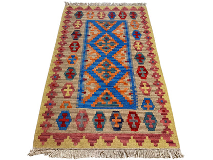 Beige kilim rug with a blue diamond pattern in the center, colorful cross border, and fringe