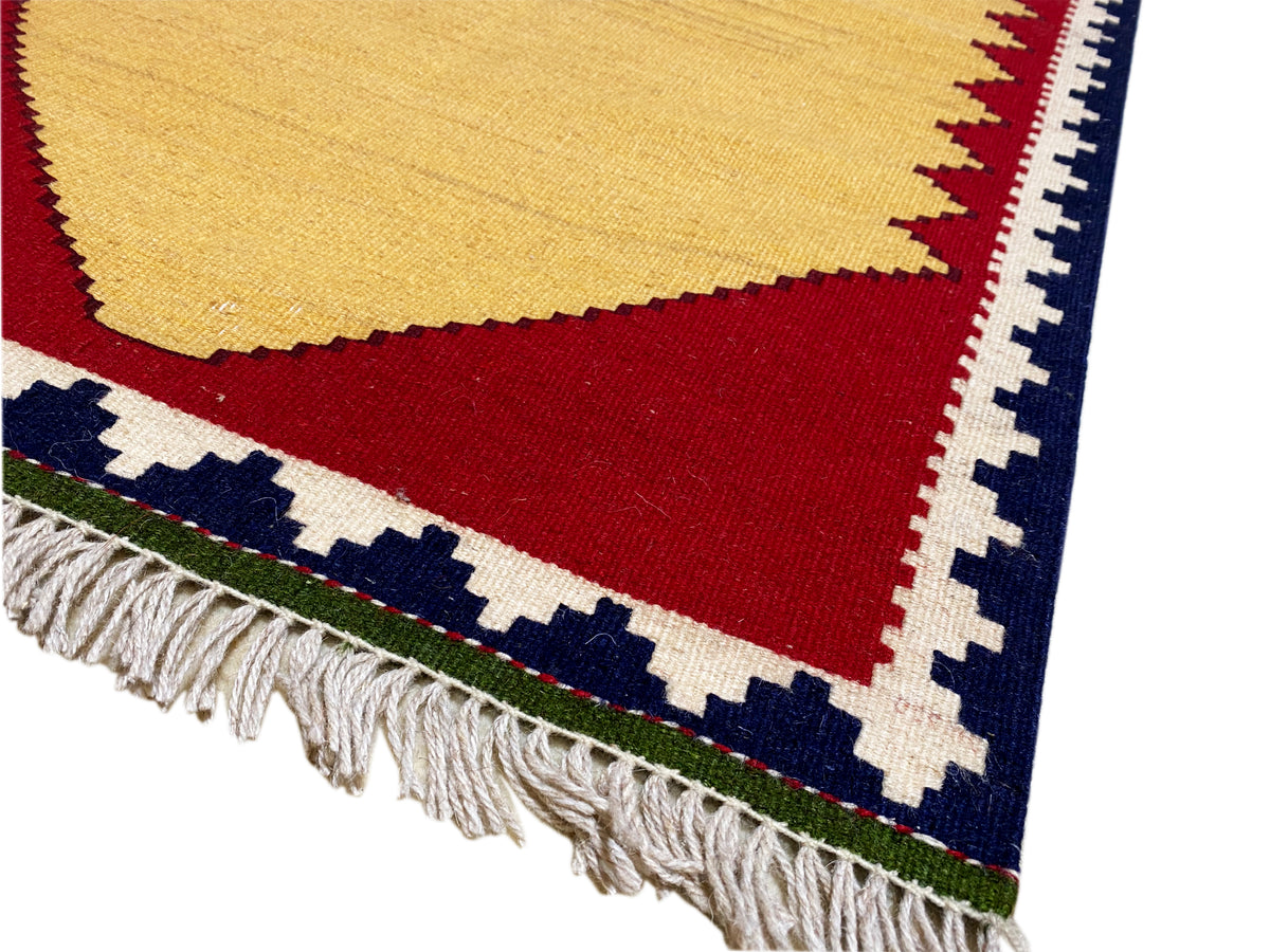 Detail of the kilim rug: fringes, red horizontal area, and blue-and-white border patterns