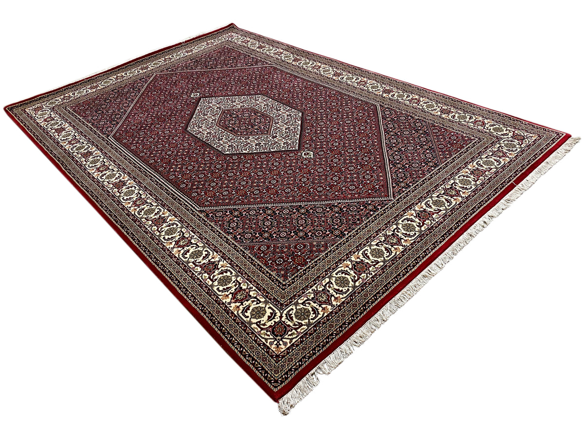 Angled photograph of a Bidjar rug with a red pattern, central medallion, and cream border