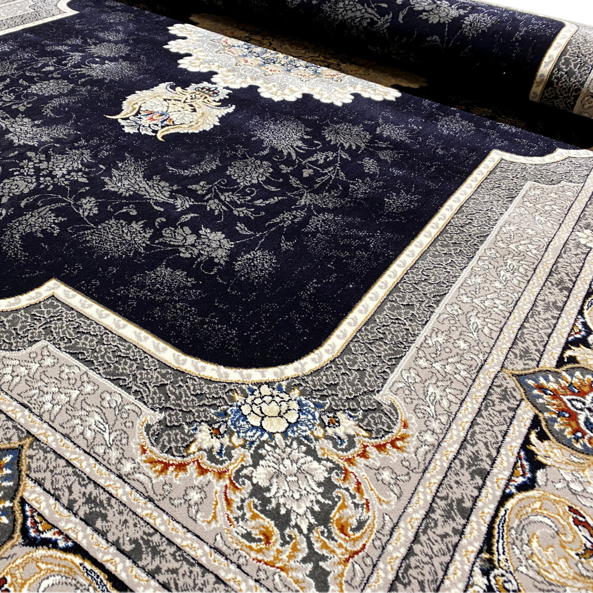 Carpet detail with dark pile and delicate tendrils in the pattern, cream-colored edging and border