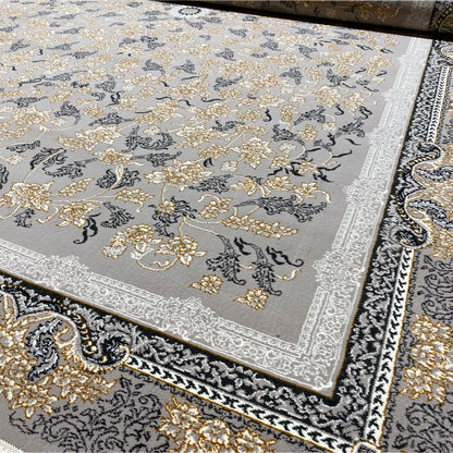 Close-up of a carpet edge with decorative trim, gold-colored floral ornaments, a gray background, and fringe