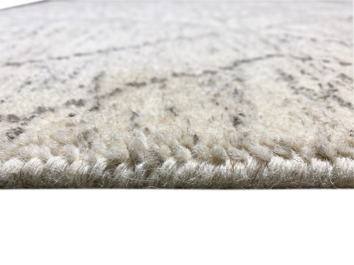 Close-up of carpet edge: dense pile in light beige with a gray marbled pattern