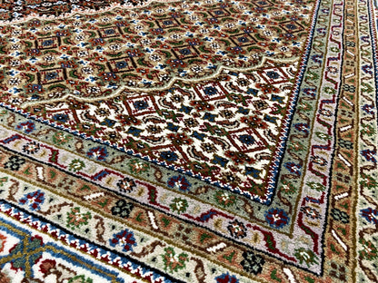 Corner of a brown Indo-Tabriz rug with colorful ornaments, decorative border, and fringe.
