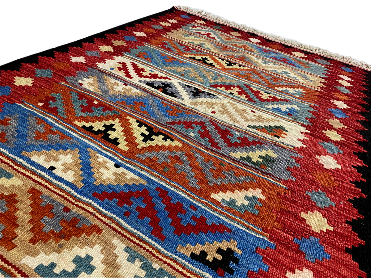 Detailed view of a kilim rug with decorative bars and a mix of patterns in red, blue, and beige.