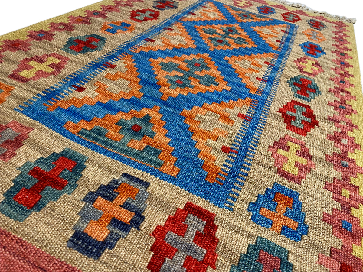 Kilim rug close-up: beige background with a blue central motif and multicolored cross ornaments
