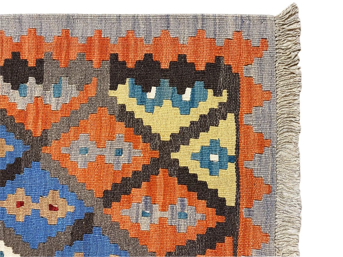 Close-up of a kilim rug: orange, blue, and cream diamonds on a gray background, frayed edges