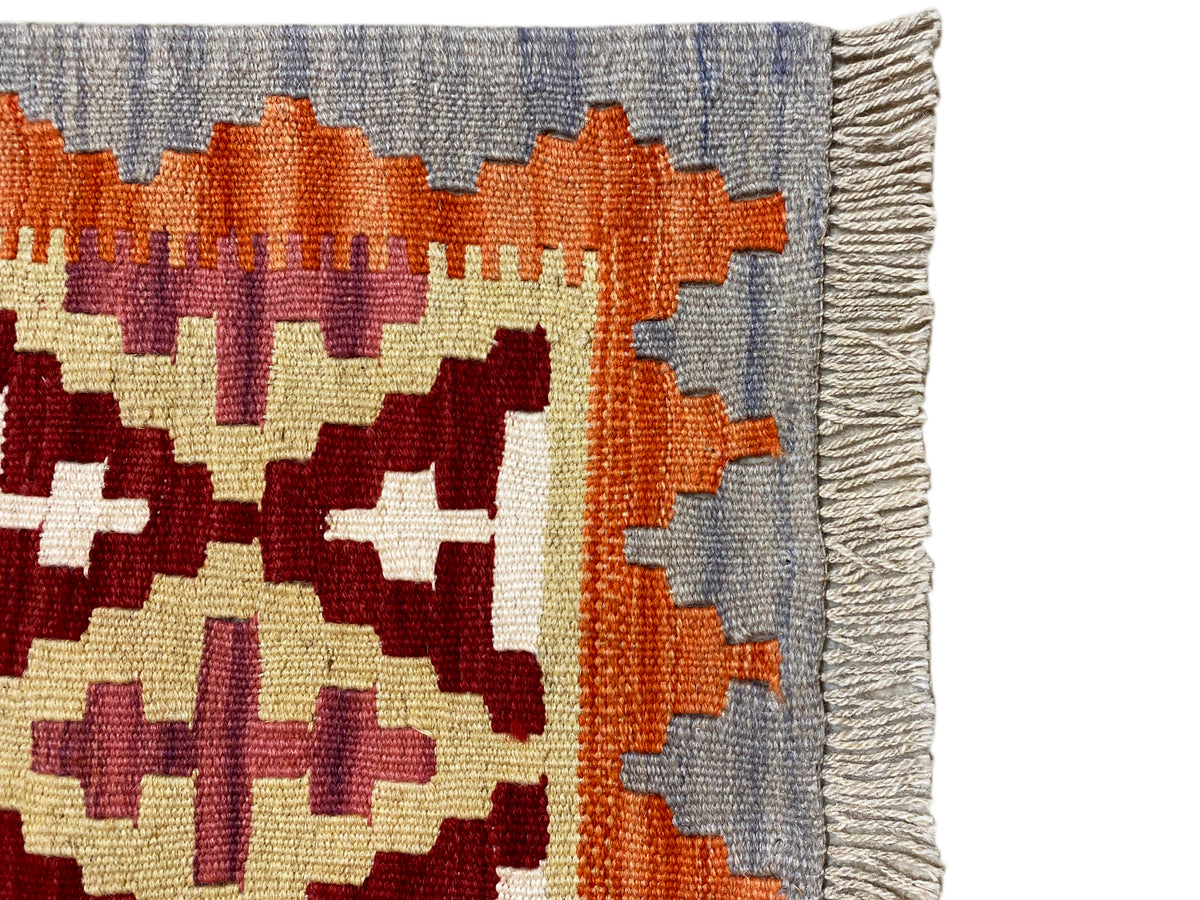 Detail of the kilim rug: fringed edges and patterns in orange, cream, and dark red on gray