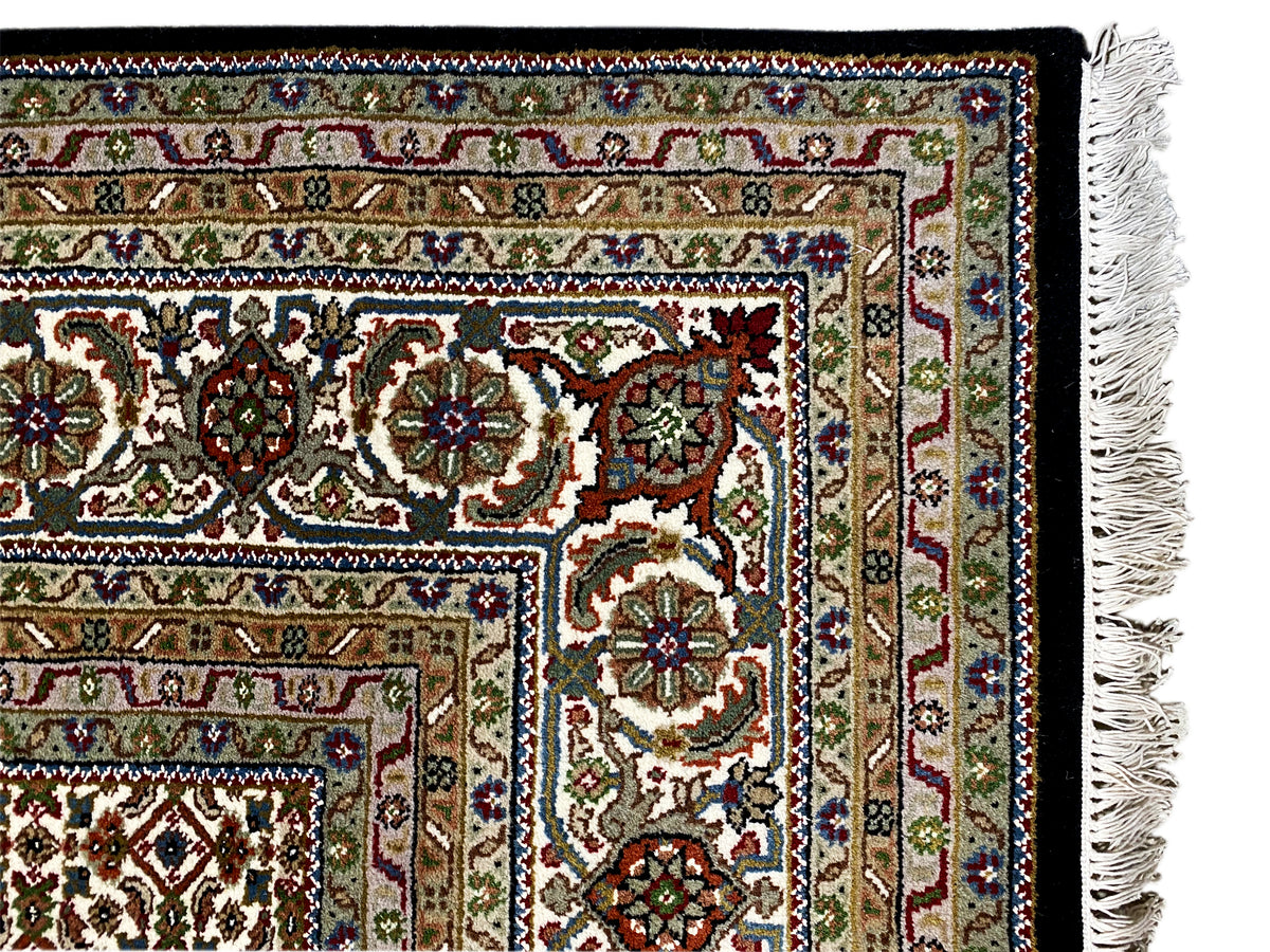 Close-up of the border of a brown Indo-Tabriz rug with floral ornaments and fringes.
