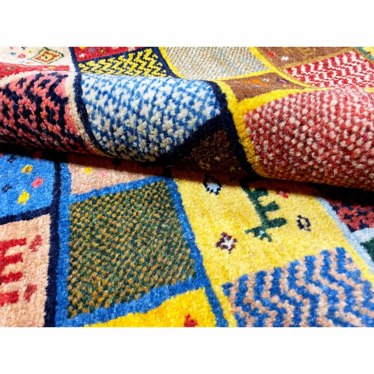 Gabbeh rug (144x125 cm) close-up: textured pile, blue-yellow and red patchwork sections.