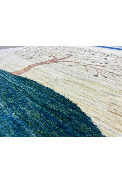 Gabbeh rug close-up: tree motif on a beige background, blue-green hill, border band