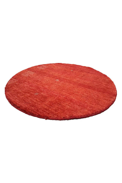 Round “Lori” Gabbeh rug (86x86 cm) in red, lying flat viewed from an oblique angle