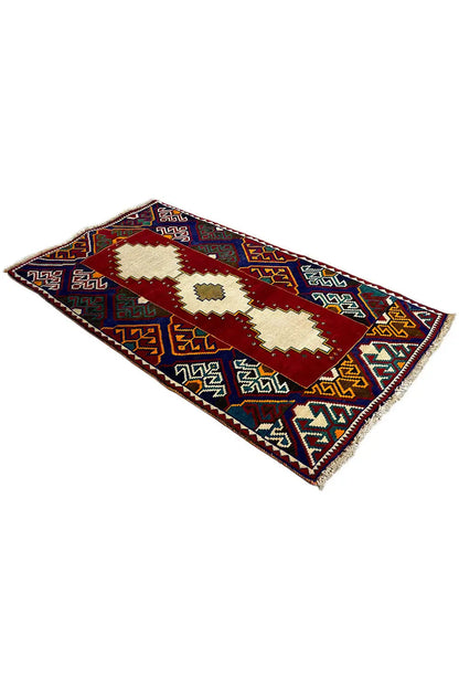 Gabbeh rug at an angle: red central band, cream ornaments, blue patterned border