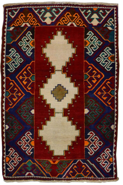 Gabbeh rug: red central medallion, blue geometric patterns, colorful border, fringes