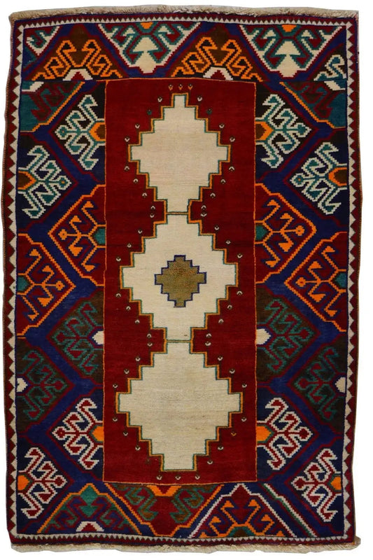 Gabbeh rug: red central medallion, blue geometric patterns, colorful border, fringes