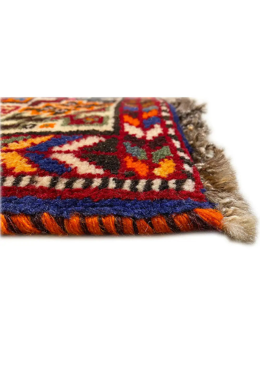 Close-up of a carpet edge with a colorful border and fringes, multicolored embroidered patterns.