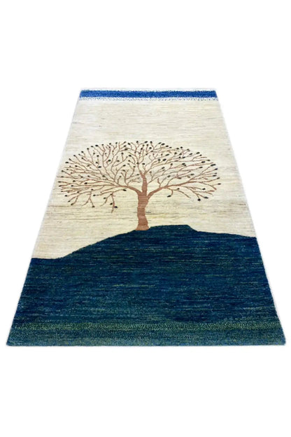Gabbeh rug with a tree design in the center, light cream background, broad dark blue area.