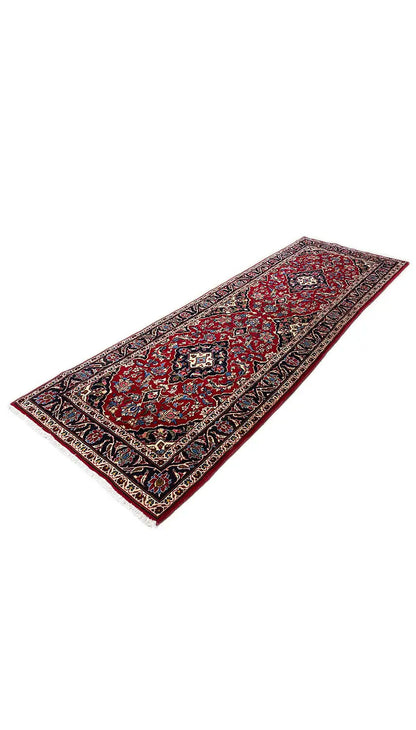 Rectangular Oriental rug in red with an ornate border, side view.