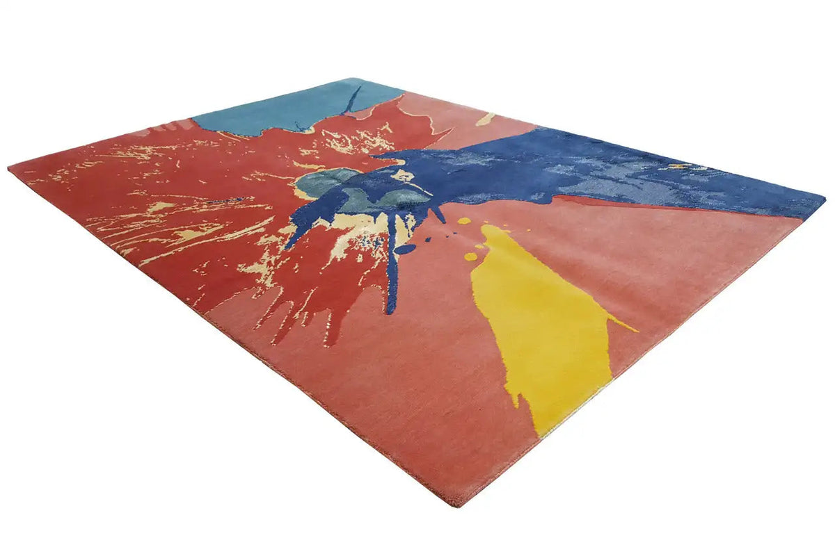 Rug with an abstract paint-splatter design in orange, blue, and yellow, viewed from above at an angle
