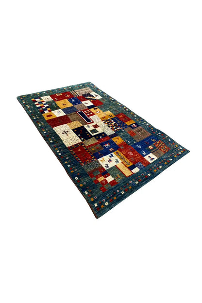Gabbeh rug (127x79 cm) shown at an angle: colorful square and line patterns on blue
