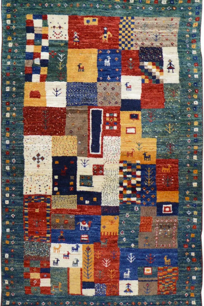 Gabbeh rug (127x79 cm) with a colorful patchwork pattern and small figures on a blue background