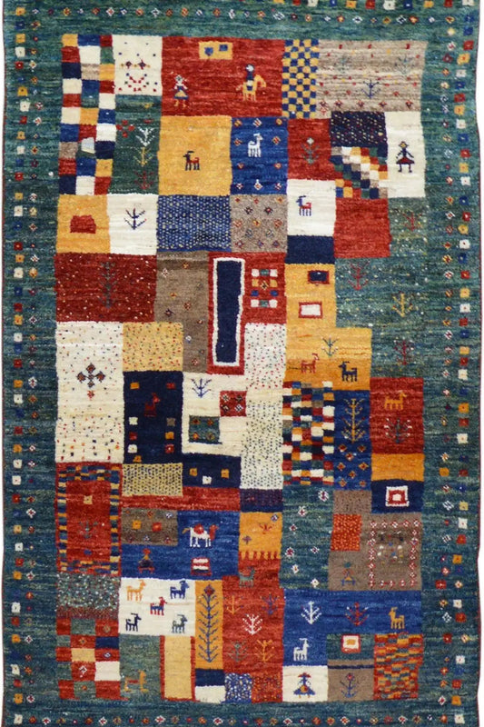 Gabbeh rug (127x79 cm) with a colorful patchwork pattern and small figures on a blue background